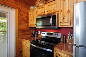 Une cuisine avec des armoires en bois, un four à micro-ondes en acier inoxydable, un four noir et un pare-feu rouge.