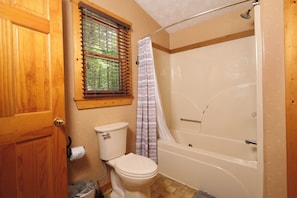 A bathroom with a toilet, a shower with a curtain, a window with blinds, and a wooden door. - Log cabin with pool table & hot tub-sleeps 8! (Pigeon Forge)