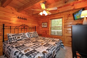 A wooden cabin bedroom with a bed, a ceiling fan, a window, and a television. - Log cabin with pool table & hot tub-sleeps 8! (Pigeon Forge)