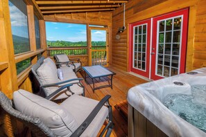A wooden deck with wicker chairs and a table, a hot tub, and a red door with glass panels. - Log cabin with pool table & hot tub-sleeps 8! (Pigeon Forge)