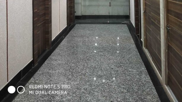 A hallway with a polished granite floor, wooden doors, and a modern ceiling design with recessed lighting.
