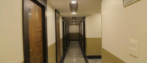 A long, narrow hallway with doors on both sides, a tiled floor, and a ceiling with recessed lighting.