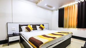 A modern hotel room with a large bed, a nightstand, a drawer, and a curtain with a gradient of yellow to black.
