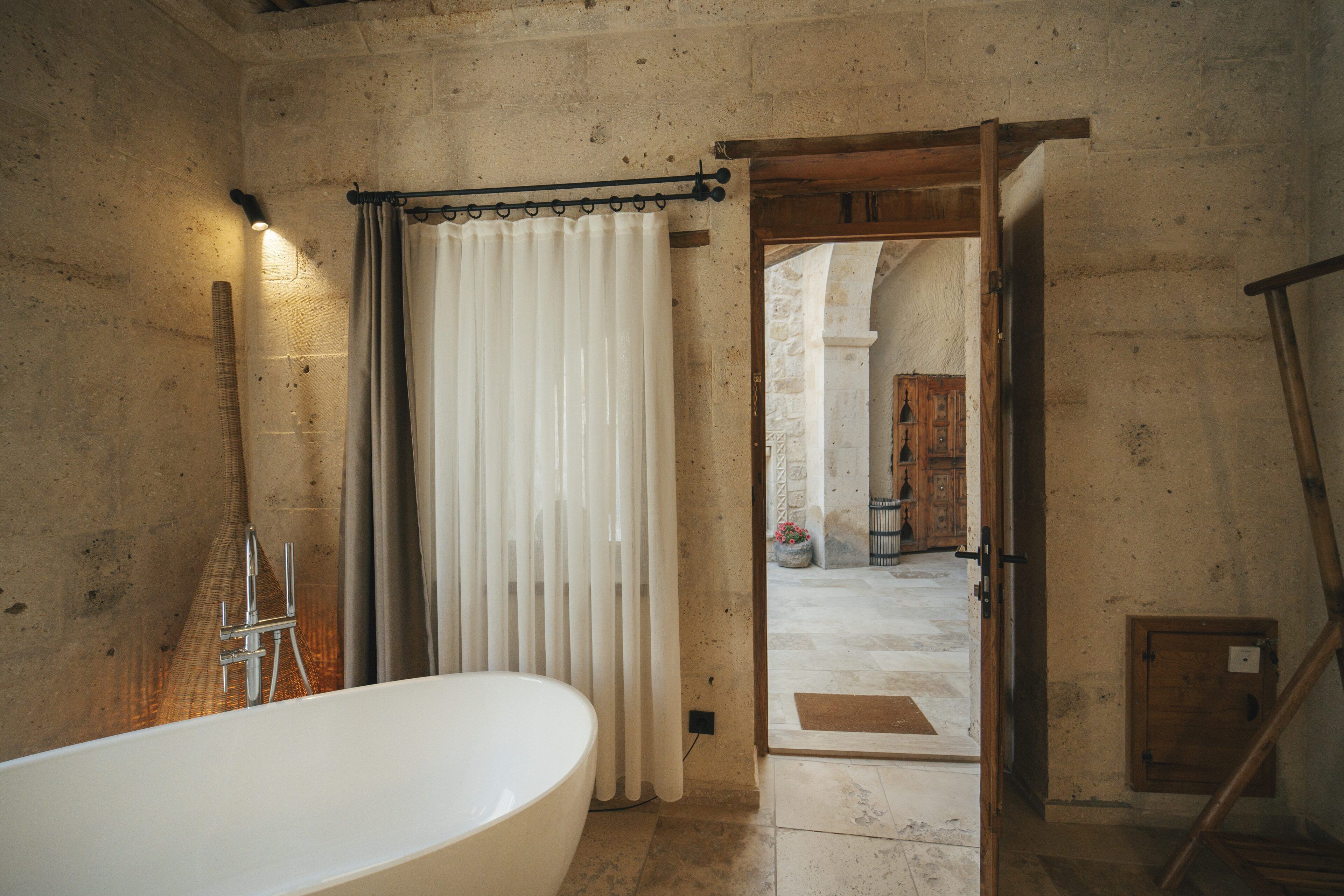A bathroom with a bathtub, a shower, and a curtain. There is a wooden door leading to another room.