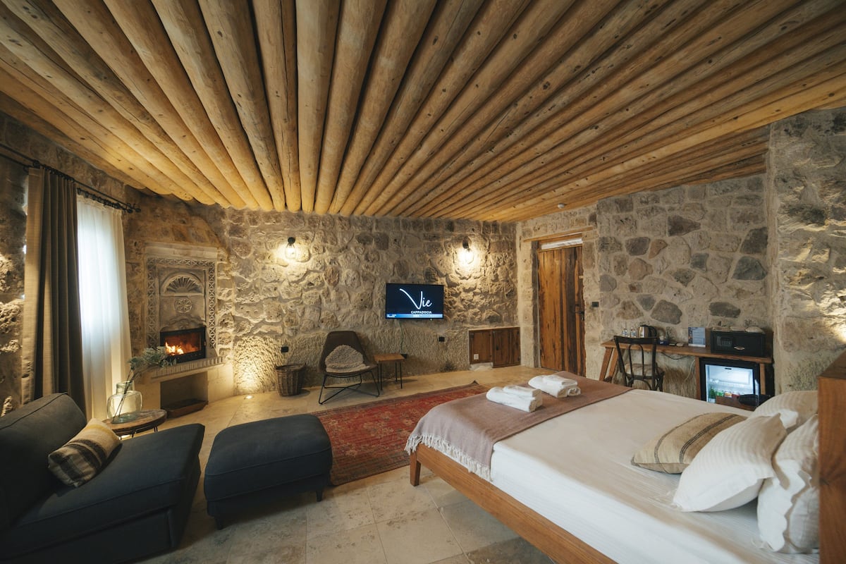 Una habitación acogedora con pared de piedra, chimenea, cama, televisor y escritorio.