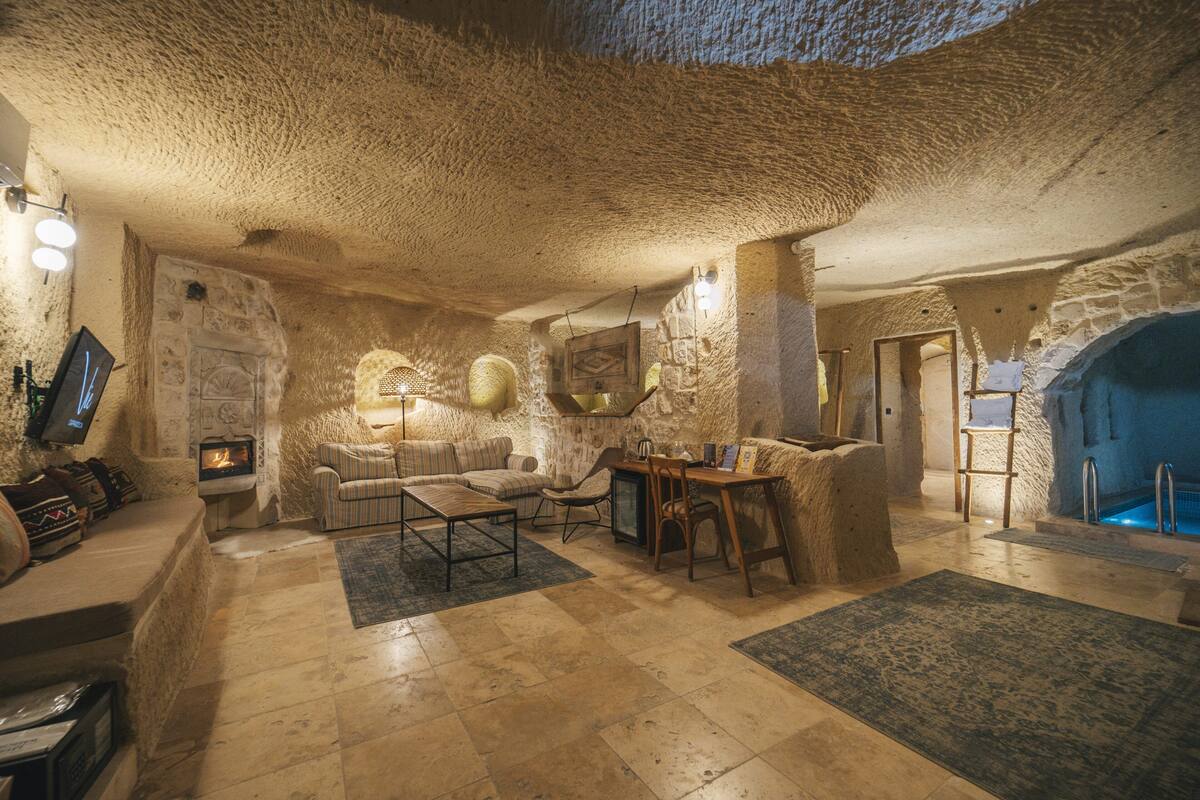 Interior de paredes de piedra con chimenea, zona de estar y una piscina.