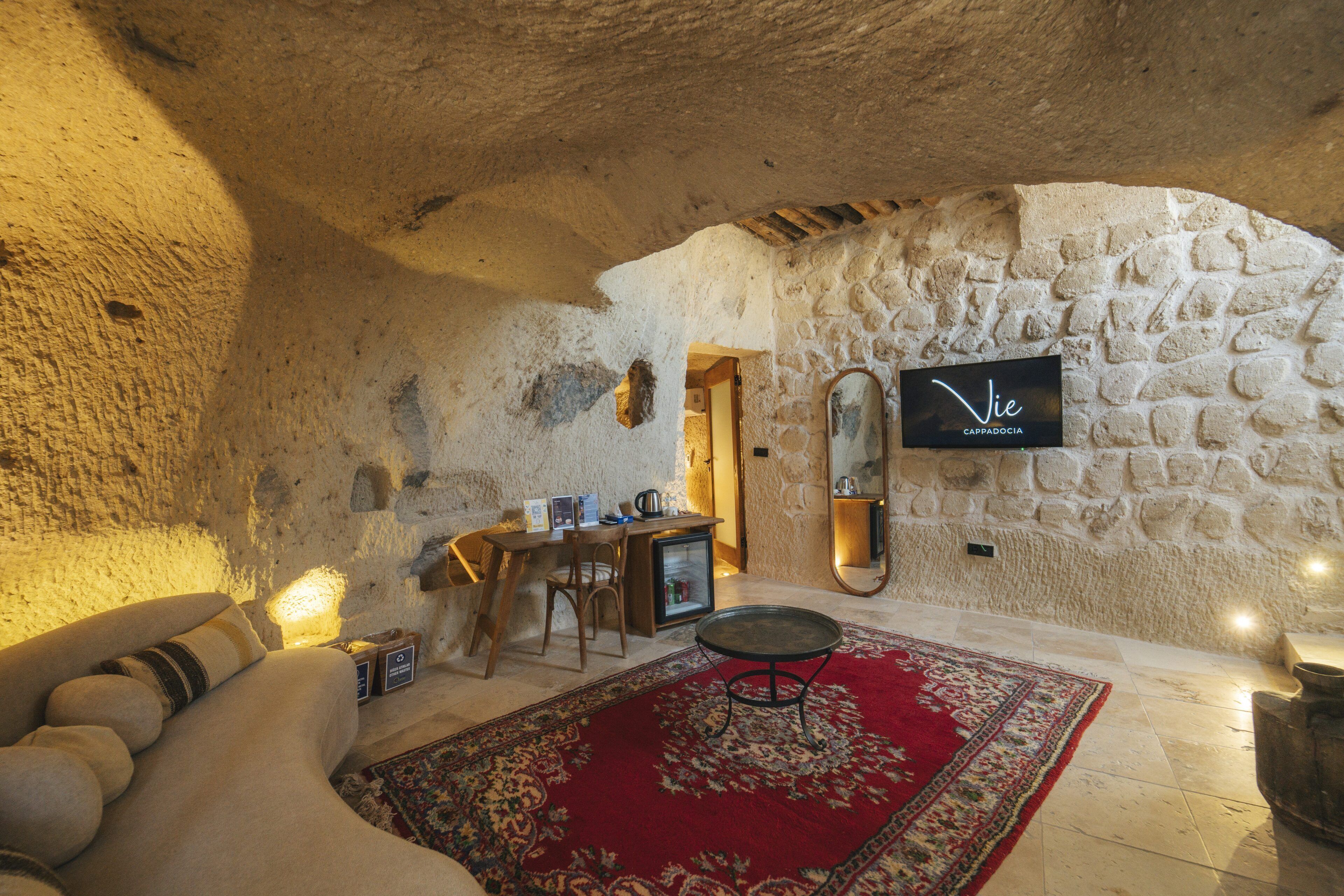 A cozy room with a stone wall, a wooden desk, a red rug, and a television mounted on the wall.