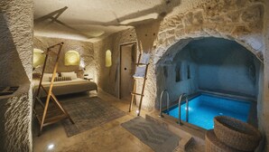 Ein Zimmer mit Steinwänden, einem Bett, einer Holzschaukel, einem kleinen Pool und einem Holzstuhl.