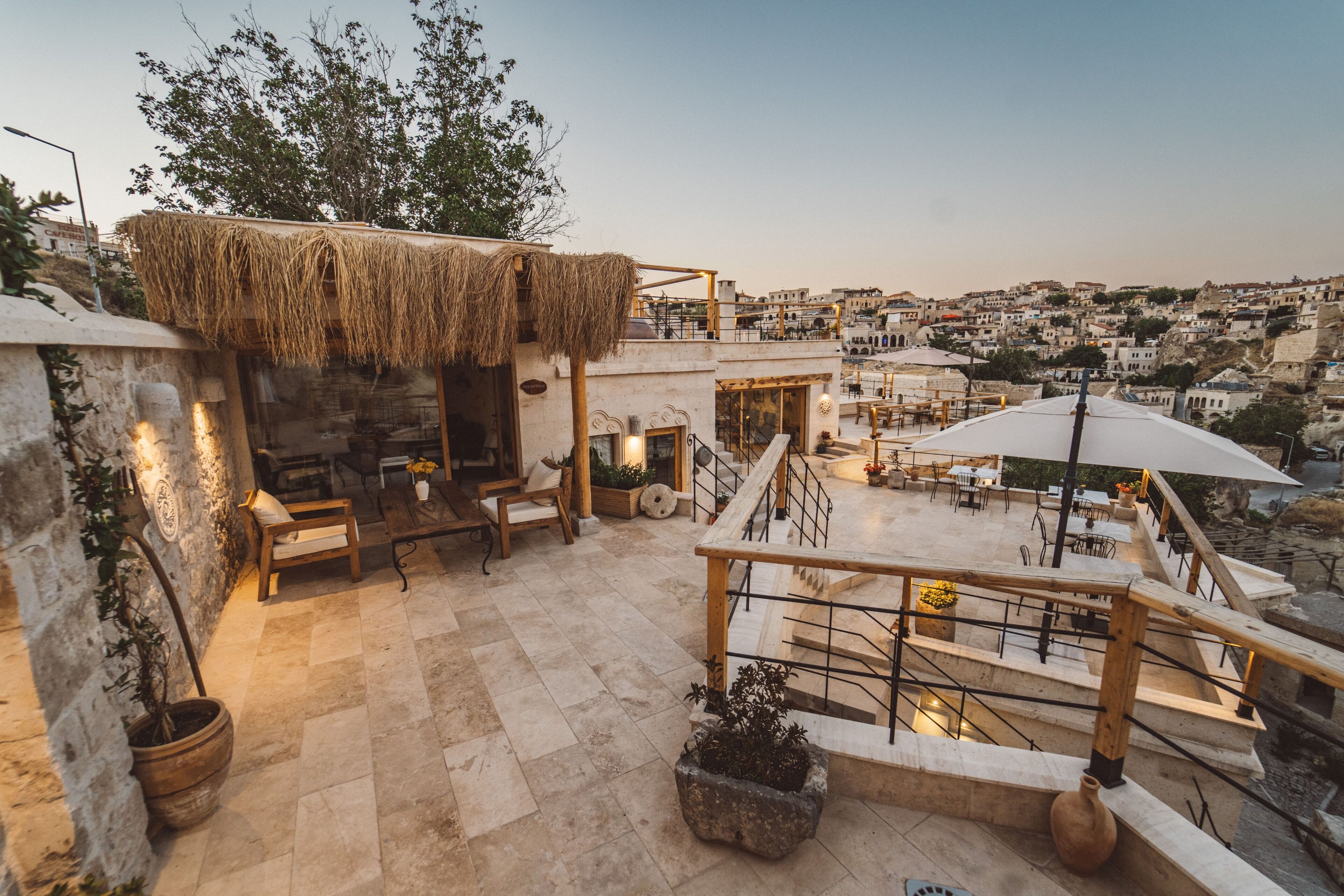A rooftop terrace with stone flooring, wooden furniture, and potted plants.