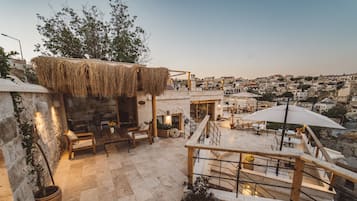 A rooftop terrace with stone flooring, wooden furniture, and potted plants.