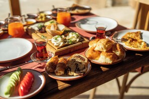 Una mesa de madera con diversos productos para el desayuno, como pan, bollería y un vaso de zumo de naranja.