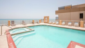 Una piscina con vista al océano, rodeada de sillas de descanso y un edificio con balcón.