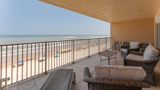 Un balcón con muebles de mimbre, vista a la playa y cielo despejado.