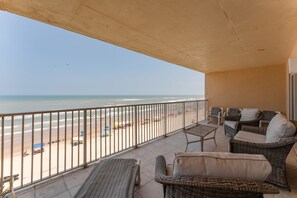 Een balkon met rieten meubels, uitzicht op het strand en een heldere lucht.