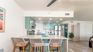 Una cocina moderna con armarios color turquesa, una isla blanca con taburetes y un refrigerador de acero inoxidable.