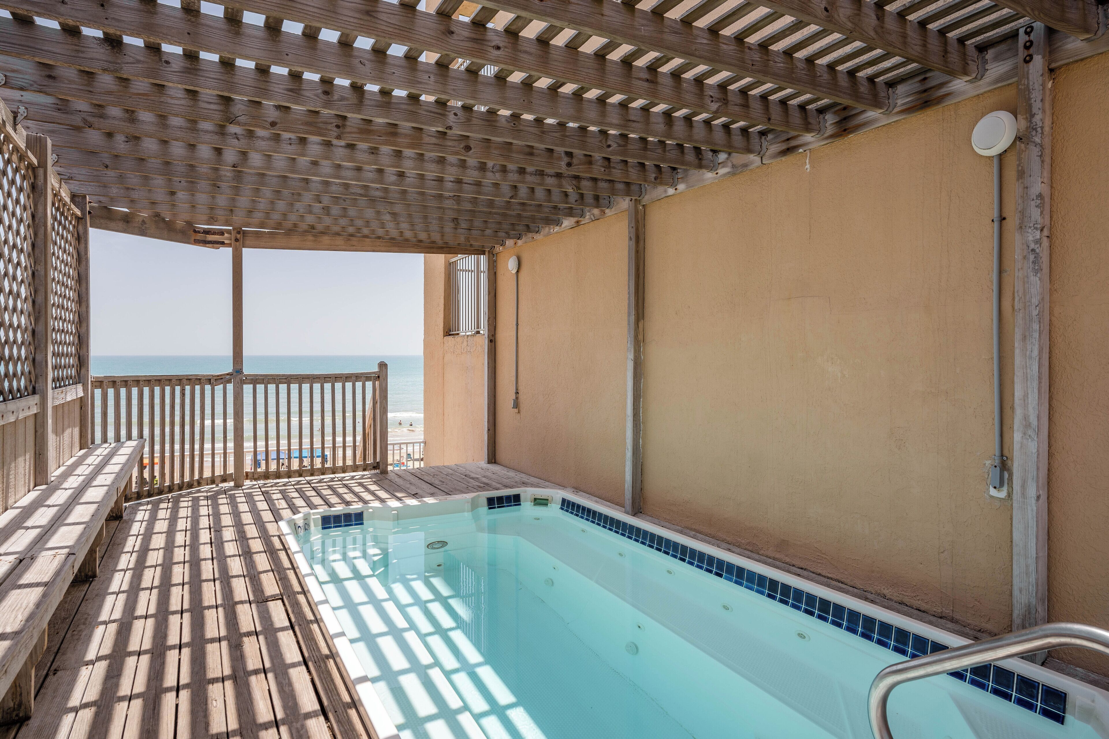A wooden deck with a pool, a wooden fence, and a view of the sea.