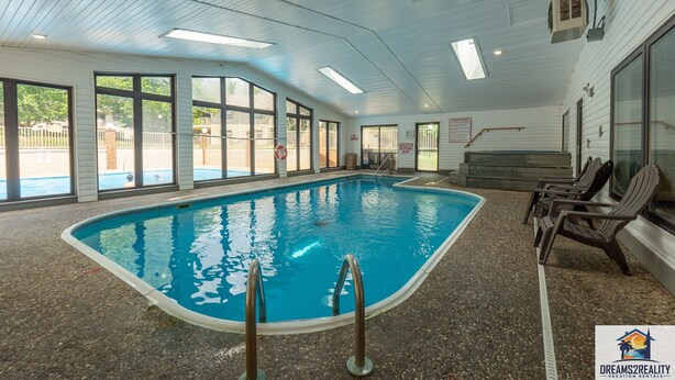 Ein Hallenbad mit großen Glaswänden, gefliestem Boden und einigen Liegestühlen.