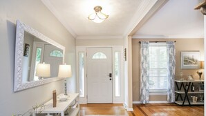 A hallway with a white door, a console table with a mirror and lamps, a blue patterned rug, and a dining area with a table and chairs. - Grand Lake Estate Luxury Waterfront Retreat (Mount Juliet)