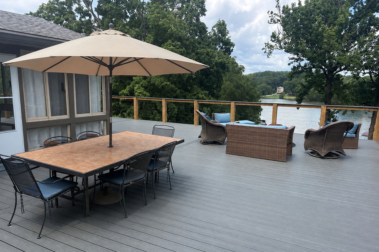 A deck with a table and chairs, a large umbrella, and wicker furniture.
