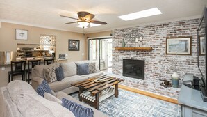 A living room with a brick fireplace, a ceiling fan, and a sofa with patterned cushions. - Grand Lake Estate Luxury Waterfront Retreat (Mount Juliet)