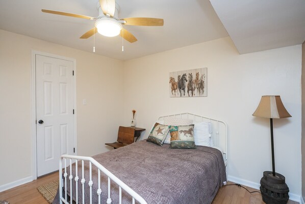 Een slaapkamer met een bed, plafondventilator, een deur, nachtkastje, lamp en een wanddecoratie.