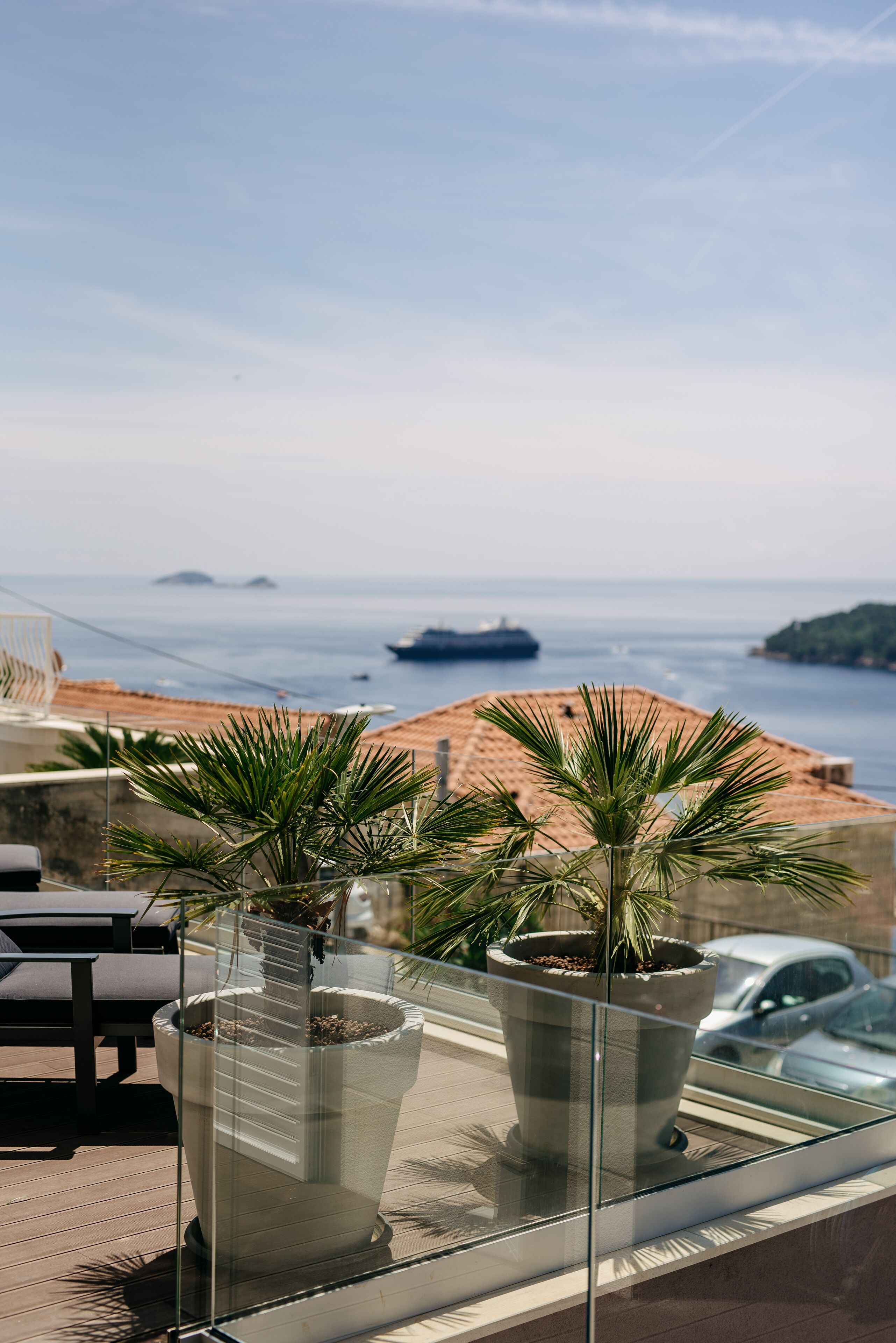 A balcony with potted plants, a view of the sea, and a distant ship.