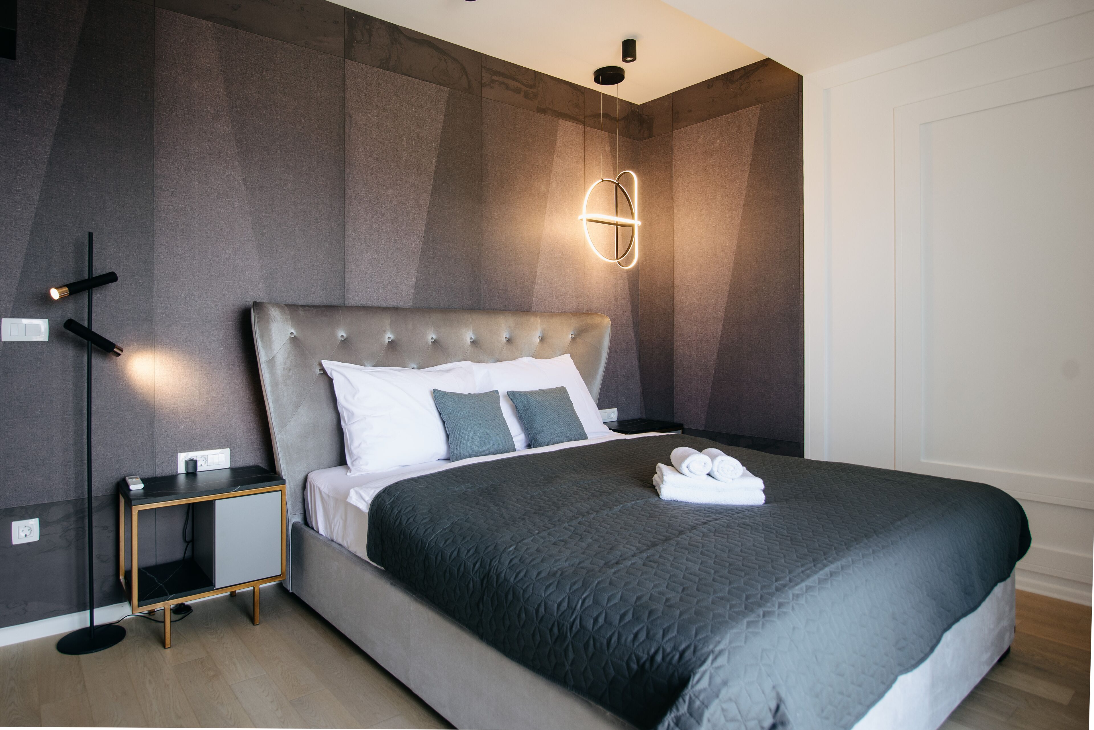 A modern bedroom with a tufted headboard, a bedside table with a lamp, and a wall-mounted light fixture.