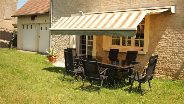 Un espacio al aire libre para comer con mesa y sillas, un toldo a rayas y un edificio de piedra al fondo.