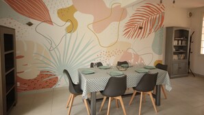 Un comedor con una mesa dispuesta para cuatro personas, rodeada de sillas. Se observa una estantería al fondo.