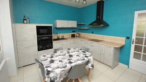 Cocina compacta con pared de acento color turquesa, horno empotrado, lavamanos y comedor con mesa preparada para dos.