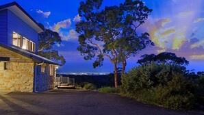 A stone building with a modern extension, a paved driveway, and a view of a cityscape at dusk. - Sydney View - 70km from Sydney; 1000km from care! (Woodford)