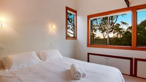 A bedroom with a large bed, a window with a view of trees, and a wall-mounted light fixture. - Sydney View - 70km from Sydney; 1000km from care! (Woodford)