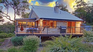 A modern house with a stone exterior, large windows, and a balcony with outdoor furniture. - Sydney View - 70km from Sydney; 1000km from care! (Woodford)