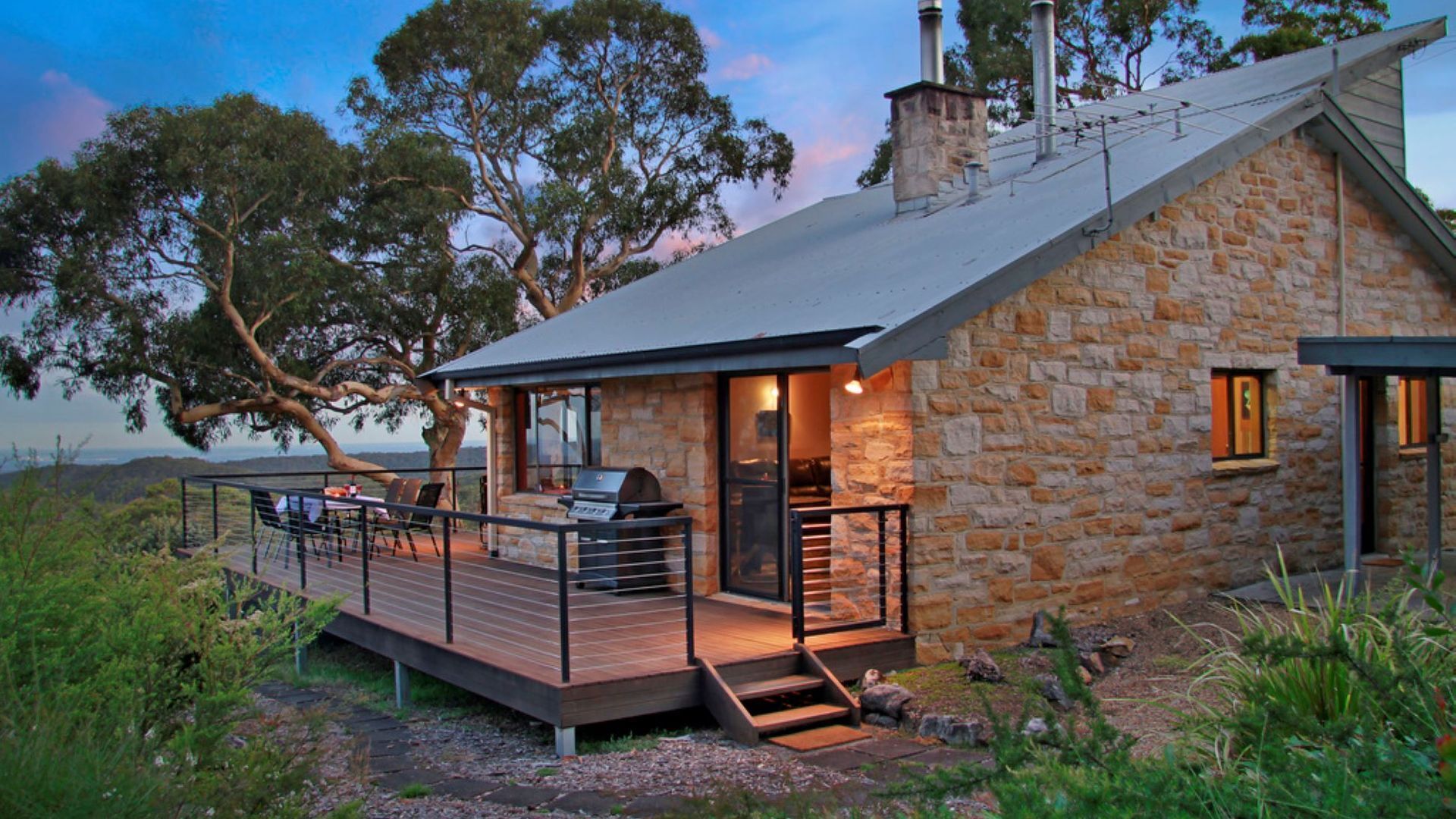 Une maison en pierre dotée d’une terrasse, d’un barbecue extérieur et de grandes fenêtres.