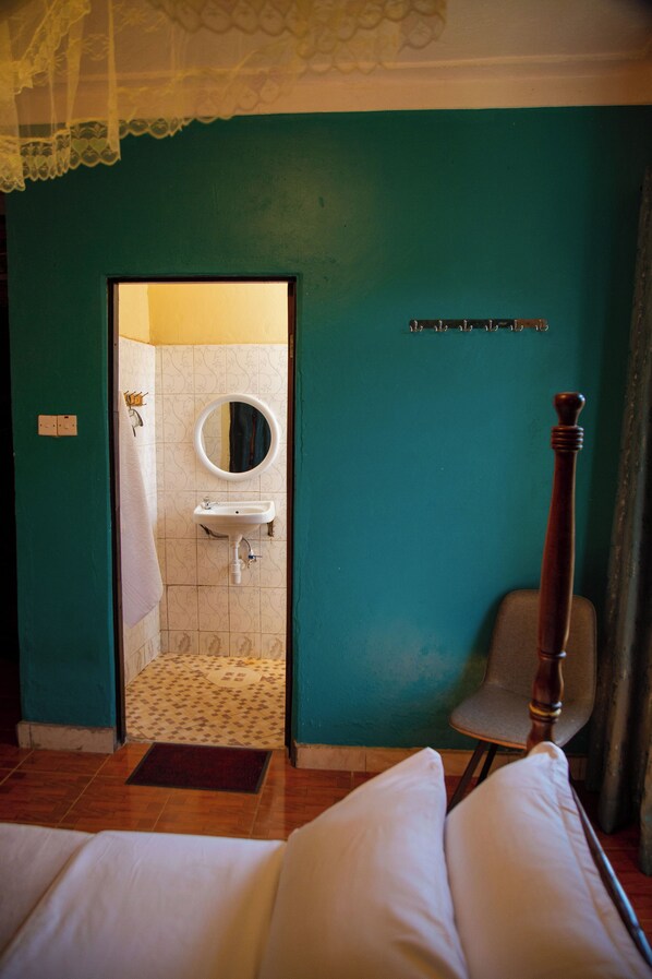 A room with a bed, a wooden chair, a bathroom with a sink and mirror, and a teal wall.
