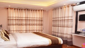 Una habitación de hotel con cama, cortinas, un televisor y una mesita con objetos encima.