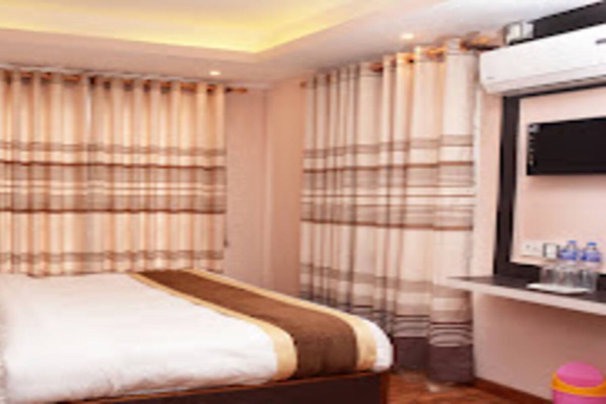Una habitación de hotel con cama, cortinas, un televisor y una mesita con objetos encima.
