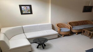 Una sala de estar con un sofá blanco, dos sillones de mimbre con cojines, una mesita redonda y dos cuadros en la pared.