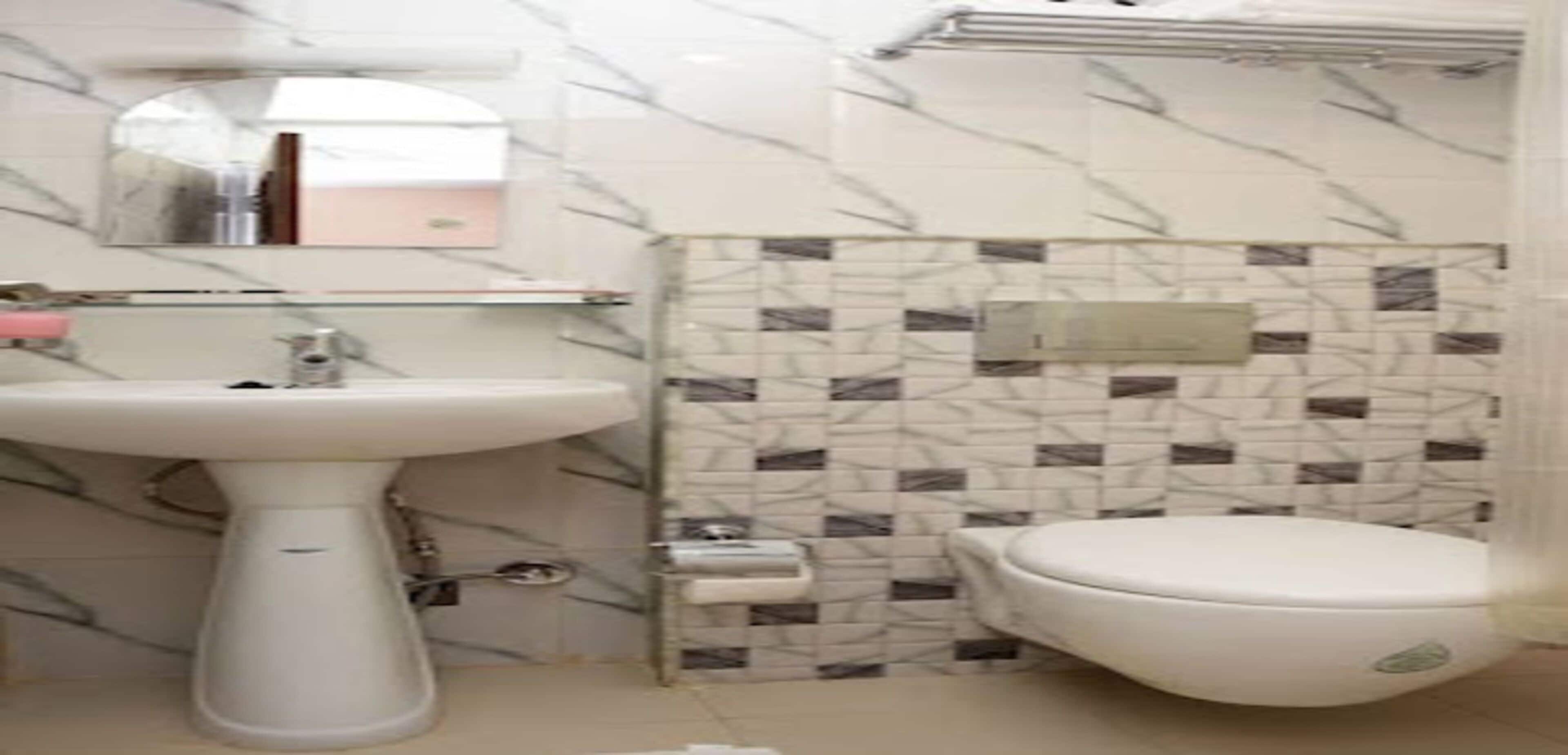 A bathroom with a white pedestal sink, a toilet, and a mirror above the sink.
