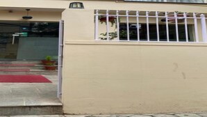 Entrada de un edificio con puerta protegida por un portón, alfombra roja y escalones que conducen a una puerta.