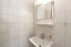 A bathroom with white tiles, a sink, a mirror, and a towel rack. - Imbarcadero apartment (Locarno)