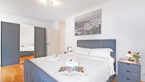 A modern hotel room with a large bed, a bedside table with a lamp, a nightstand, and a framed cityscape picture on the wall. - Imbarcadero apartment (Locarno)