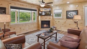 A cozy cabin interior with a fireplace, leather sofas, a coffee table, and a ceiling fan. - Rocky Flats Haven (Cosby)