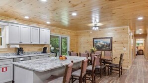 A wooden cabin interior with a kitchen, dining area, and a large window. - Rocky Flats Haven (Cosby)