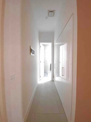 A narrow, well-lit hallway with white walls and a tiled floor, leading to a bright room with a door at the end. - Light Filled Fitzroy North Home + Free Street Parking, Balcony (Fitzroy North)