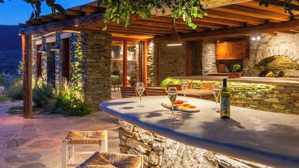 An outdoor patio area with stone walls, wooden furniture, and a stone fireplace.