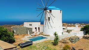 A windmill with a pool and stone buildings, overlooking a coastal landscape.