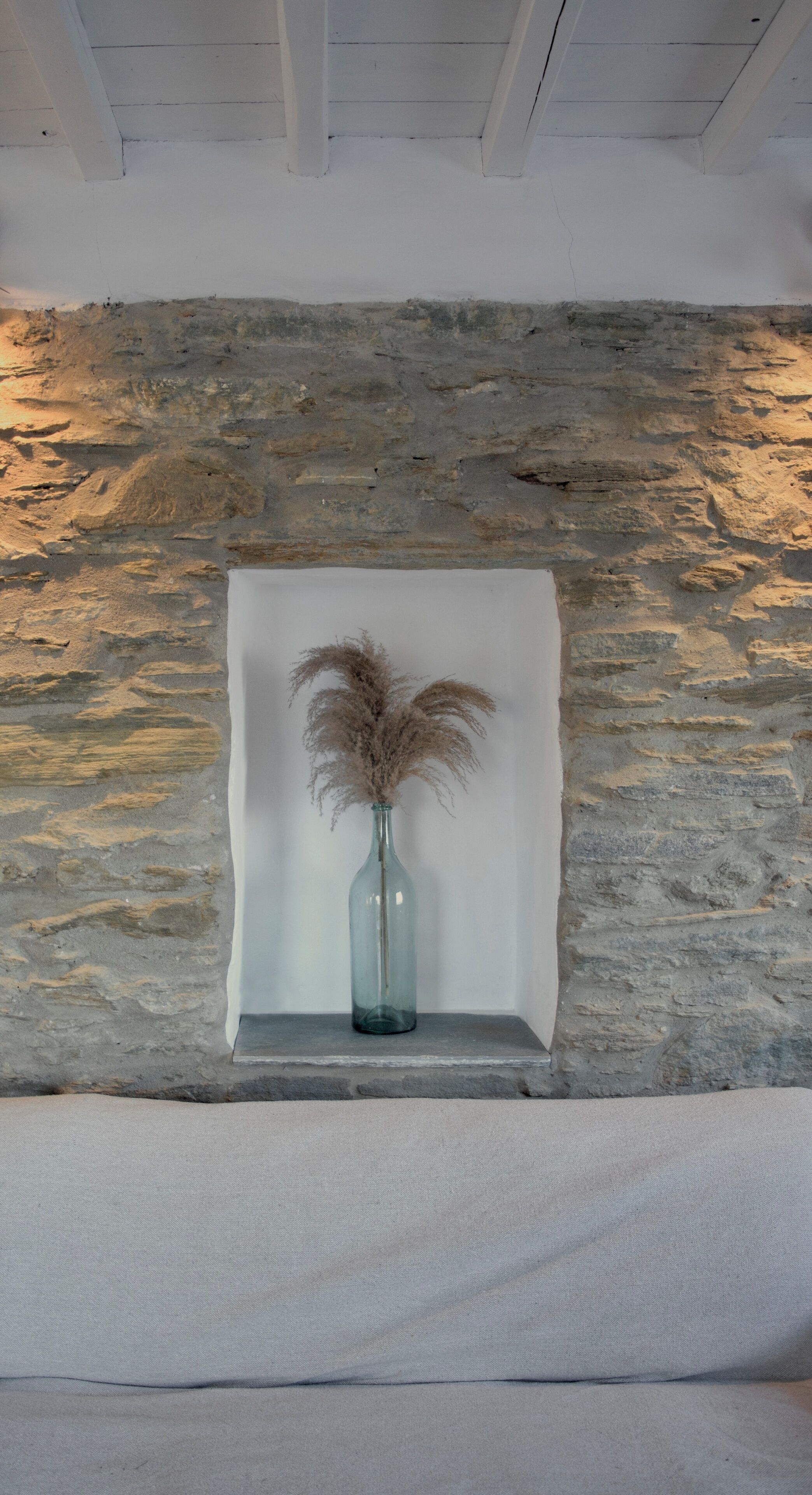 A stone wall with a framed picture of pampas grass in a glass vase on a shelf.