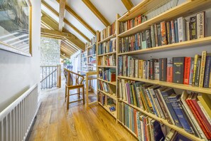 A library with wooden bookshelves filled with books, a wooden chair, and a staircase leading to an upper level.