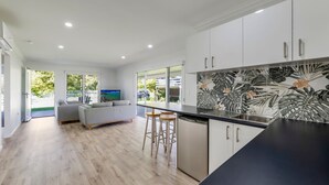 A modern kitchen with a black countertop, white cabinets, and a large window overlooking a garden.